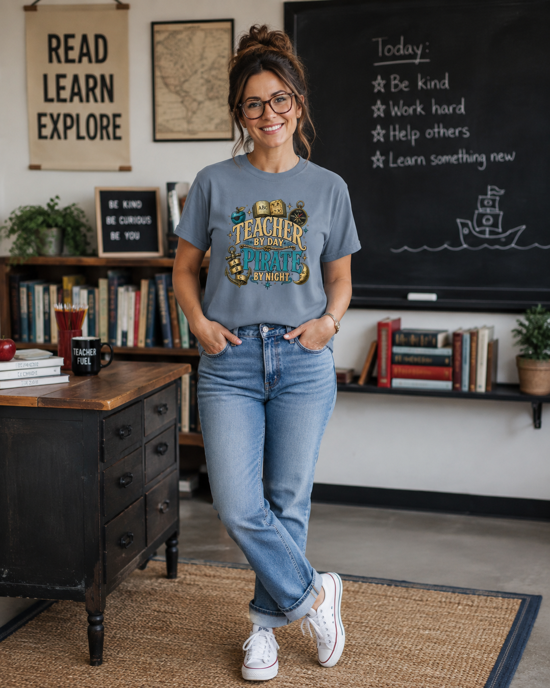 Teacher by Day Pirate by Night shirt: gold and teal lettering with an ABC storybook, compass and anchor, worn by a teacher standing in her classroom