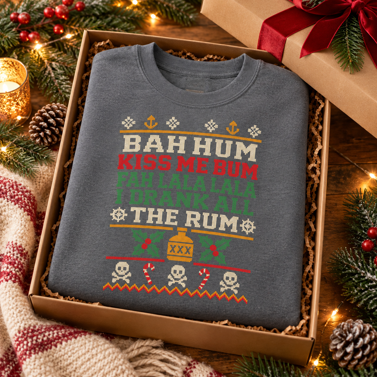 Charcoal Bah Hum Kiss Me Bum sweatshirt folded in a gift box with pine cones and a red ribbon