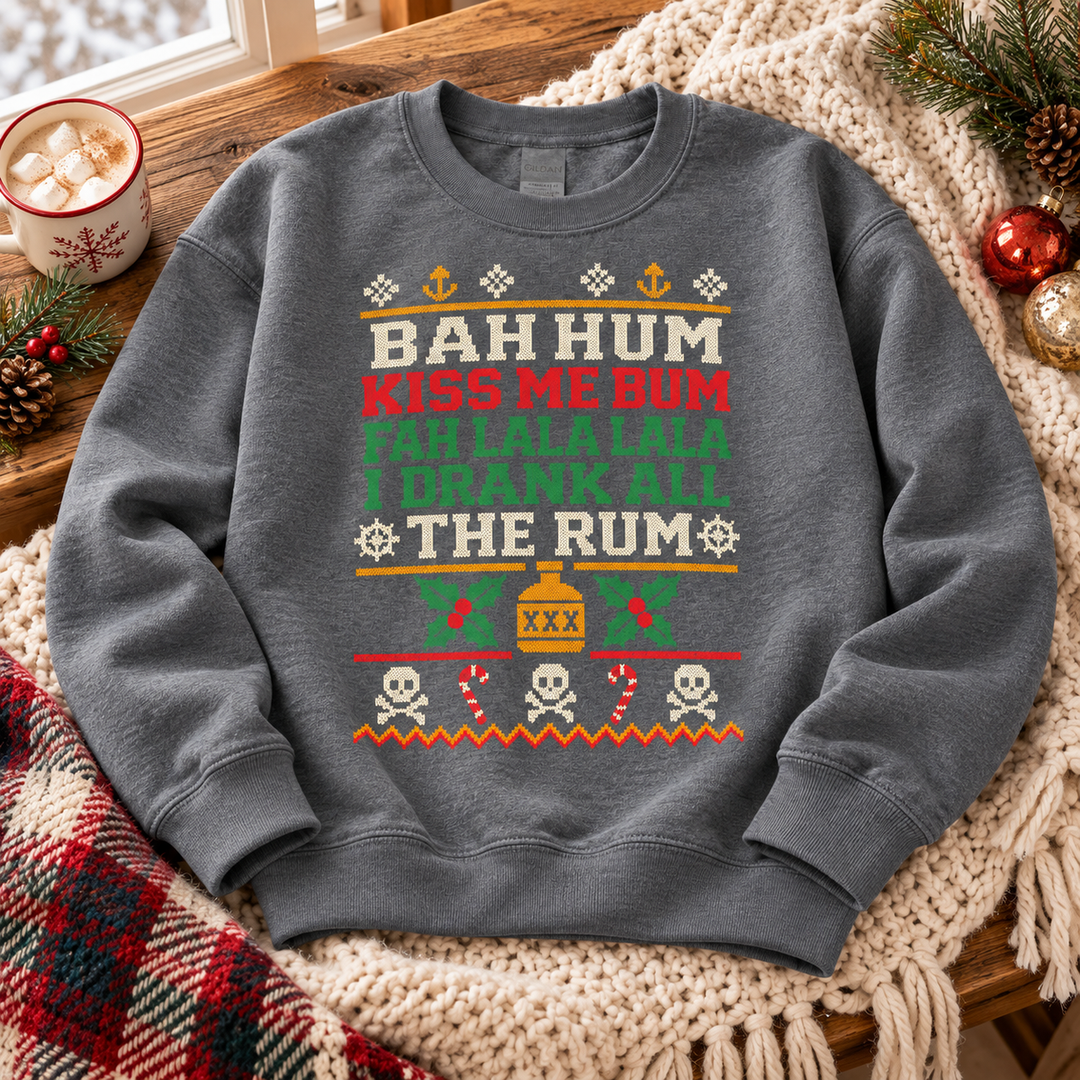 Dark Heather Bah Hum Kiss Me Bum sweatshirt laid on a knit throw beside a mug of hot cocoa