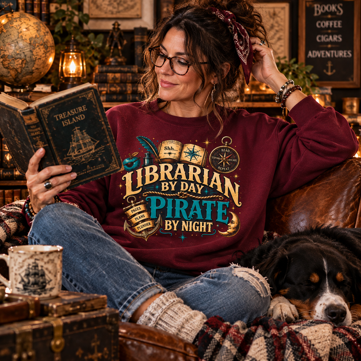 Woman in a maroon Librarian by Day Pirate by Night sweatshirt reading on a couch with her dog