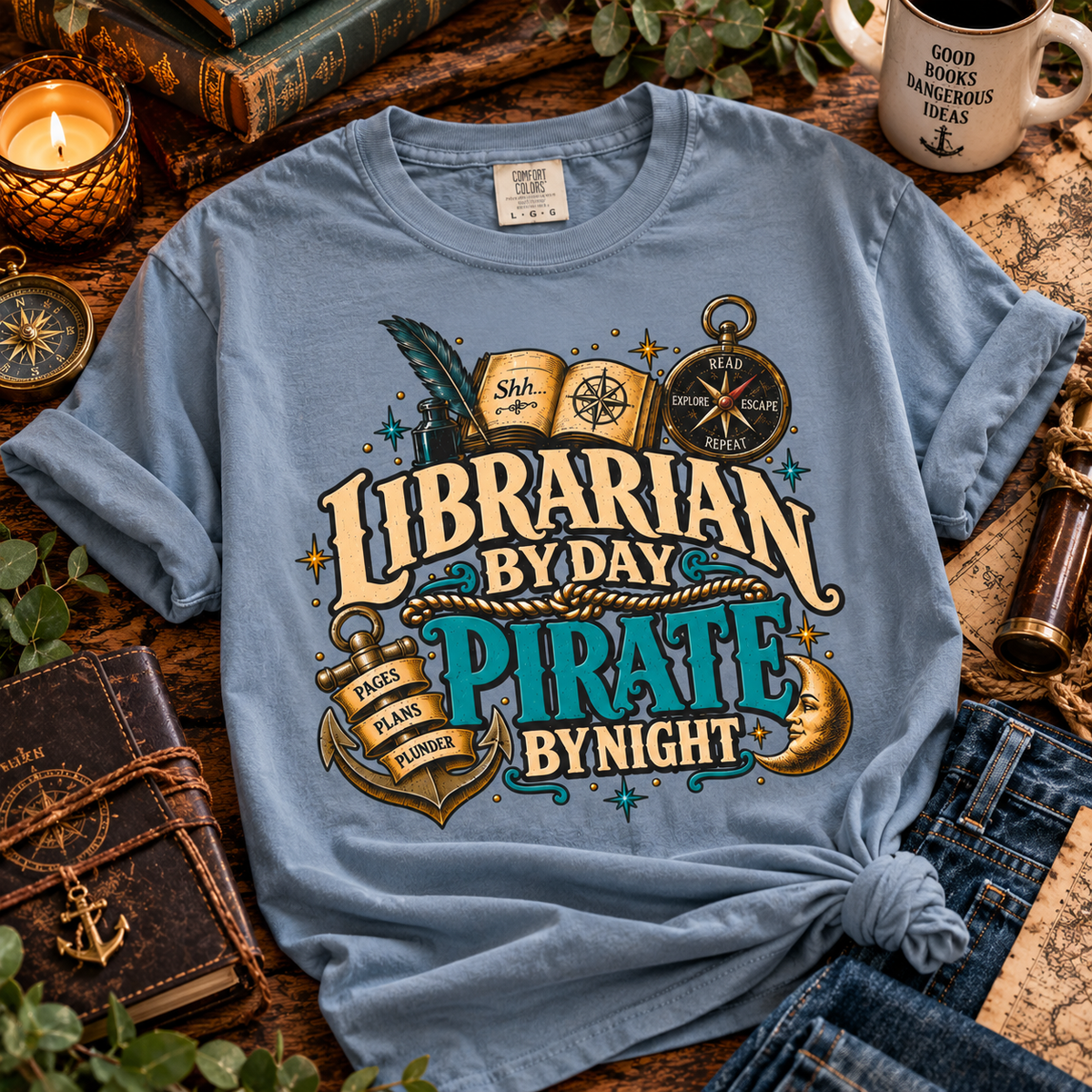 Light blue Librarian by Day Pirate by Night t-shirt laid out on a desk with a map, candles and a coffee mug