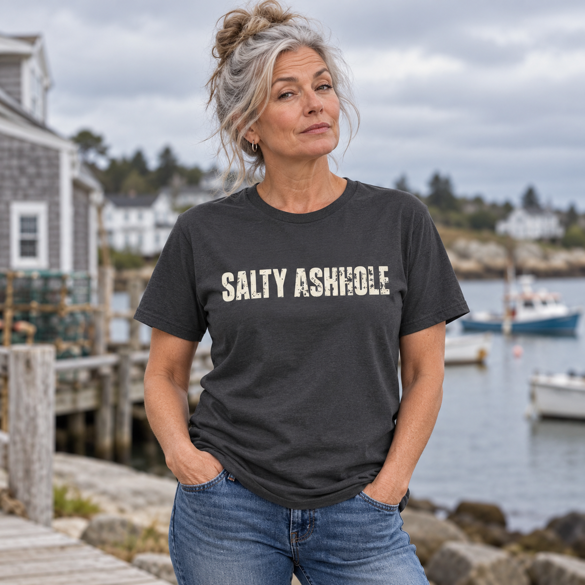 Woman on a harbor dock wearing a charcoal Salty Ashhole tee, boats in the water behind her